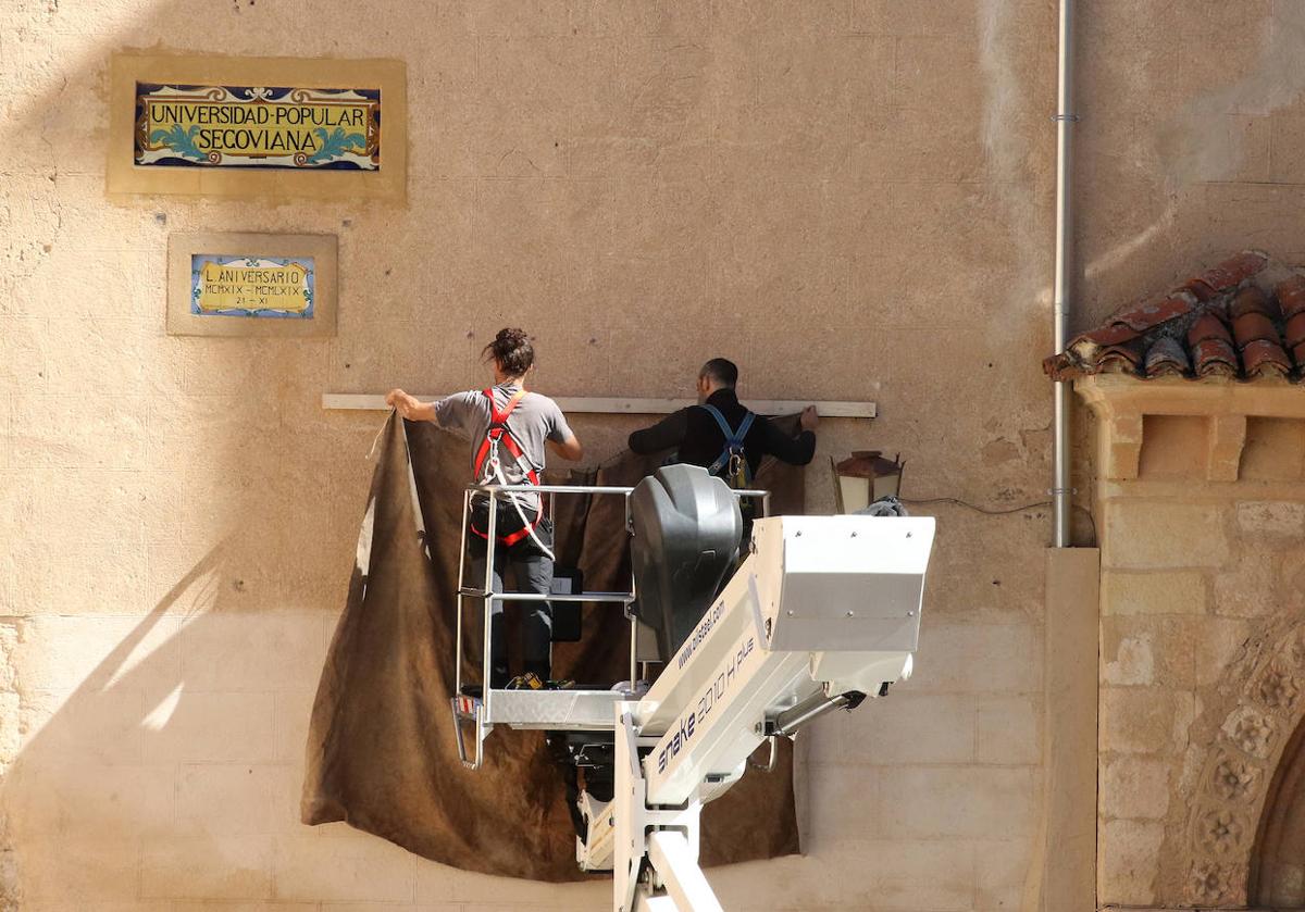 Dos trabajadores tapan el letrero de la Real Academia de Historia y Arte de San Quirce.