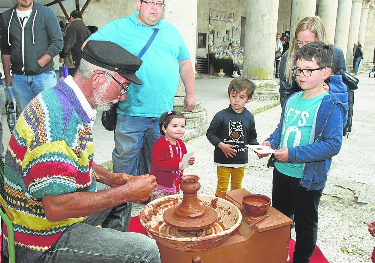 El público, en el que destacan varios pequeños, contempla el trabajo de un alfarero en la feria.