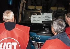 Participantes en un piquete observan un autobús con cartel de servicios mínimos.