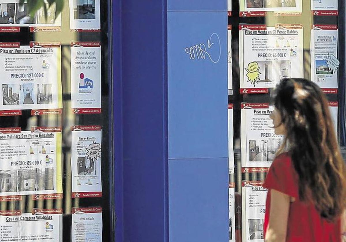 Una mujer observa varios anuncios de alquiler y venta de pisos en el escaparate de una inmobiliaria de Valladolid.