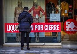 Una mujer mira el escaparate de un comercio en liquidación.