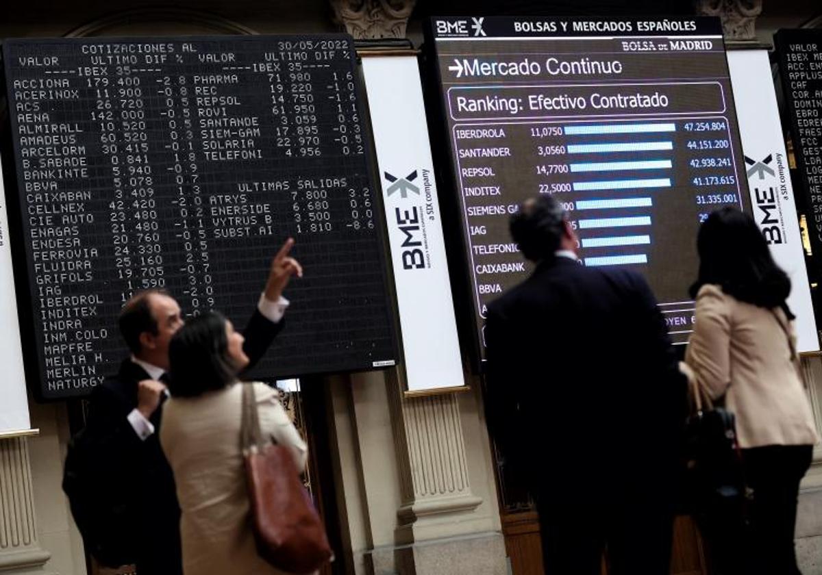 Cuatro personas frente a un panel de valores del Ibex 25 en el Palacio de la Bolsa, en Madrid.