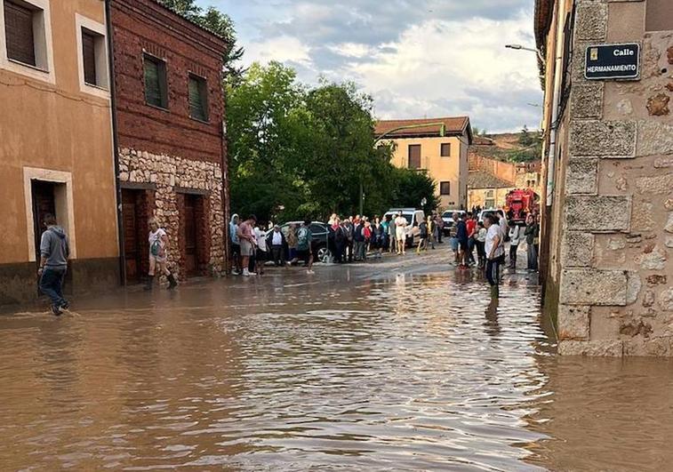 Vecinos tratan de sortear una balsa de agua y barro en Ayllón tras la tromba de este domingo.