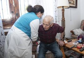 Una trabajadora auxiliar del servicio de ayuda a domicilio presta asistencia a un hombre para levantarse.