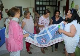 La alcaldesa, Sara Esteban, con varias mujeres voluntarias, muestran un mantel artesanal.