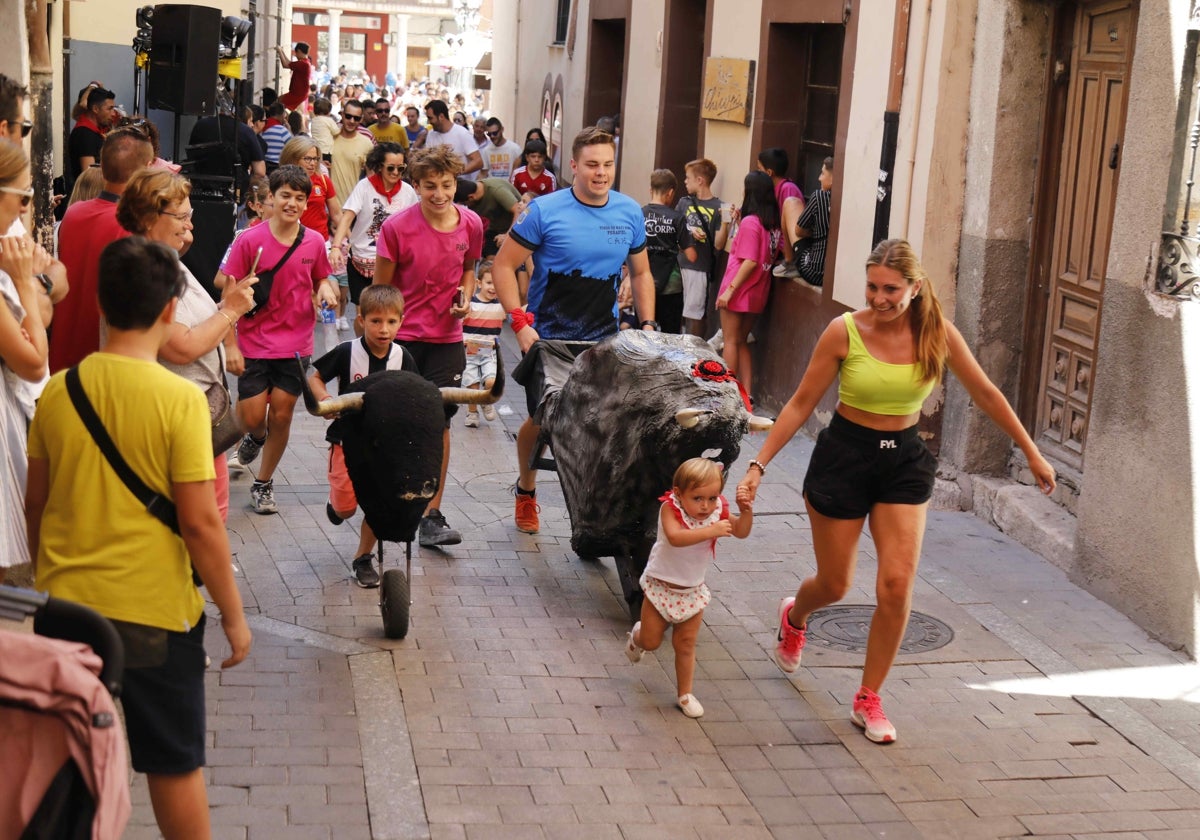 Una niña participa con su madre en el encierro de los toros de juguete.