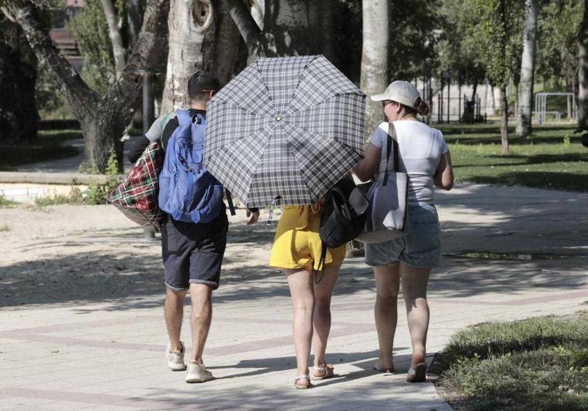 Tres jóvenes se protegen del sol con un paraguas en el entorno de Las Moreras.