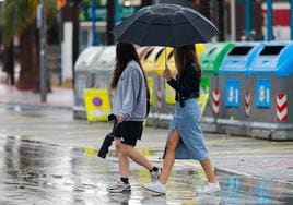 Dos chicas caminan por la calle bajo un paraguas.