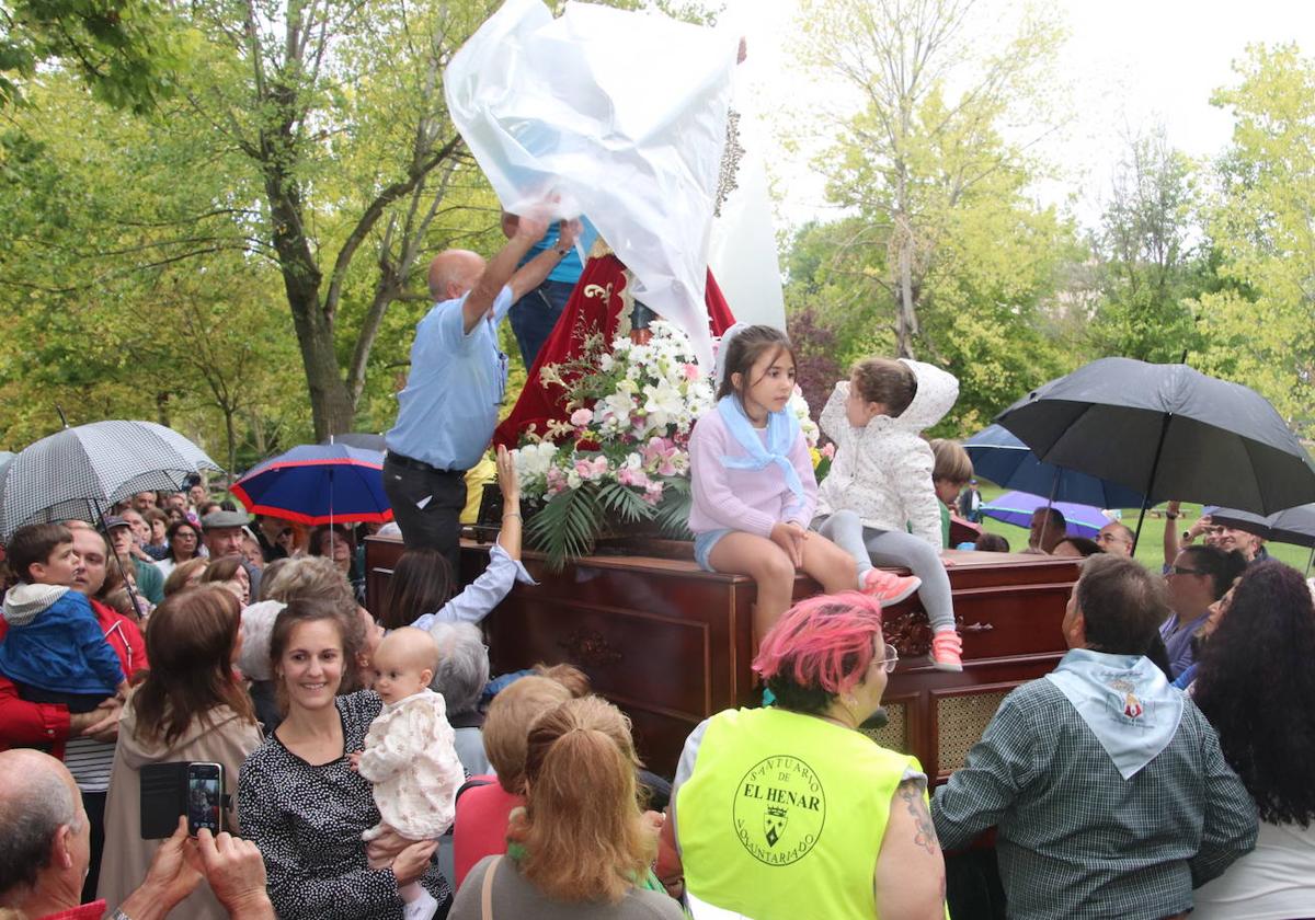 Dos personas cubren la imagen de la Virgen con un plástico para protegerla de la lluvia durante la procesión.