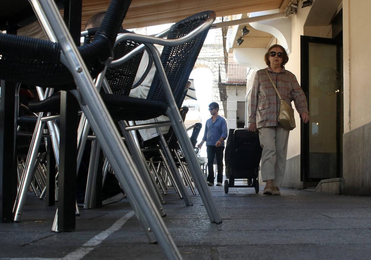 Una mujer pasea junto a las sillas de la terraza de un bar de la ciudad de Segovia.