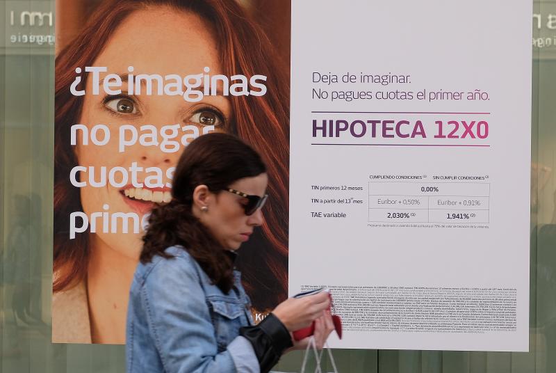 Una mujer camina junto a un escaparate con un anuncio de hipotecas.