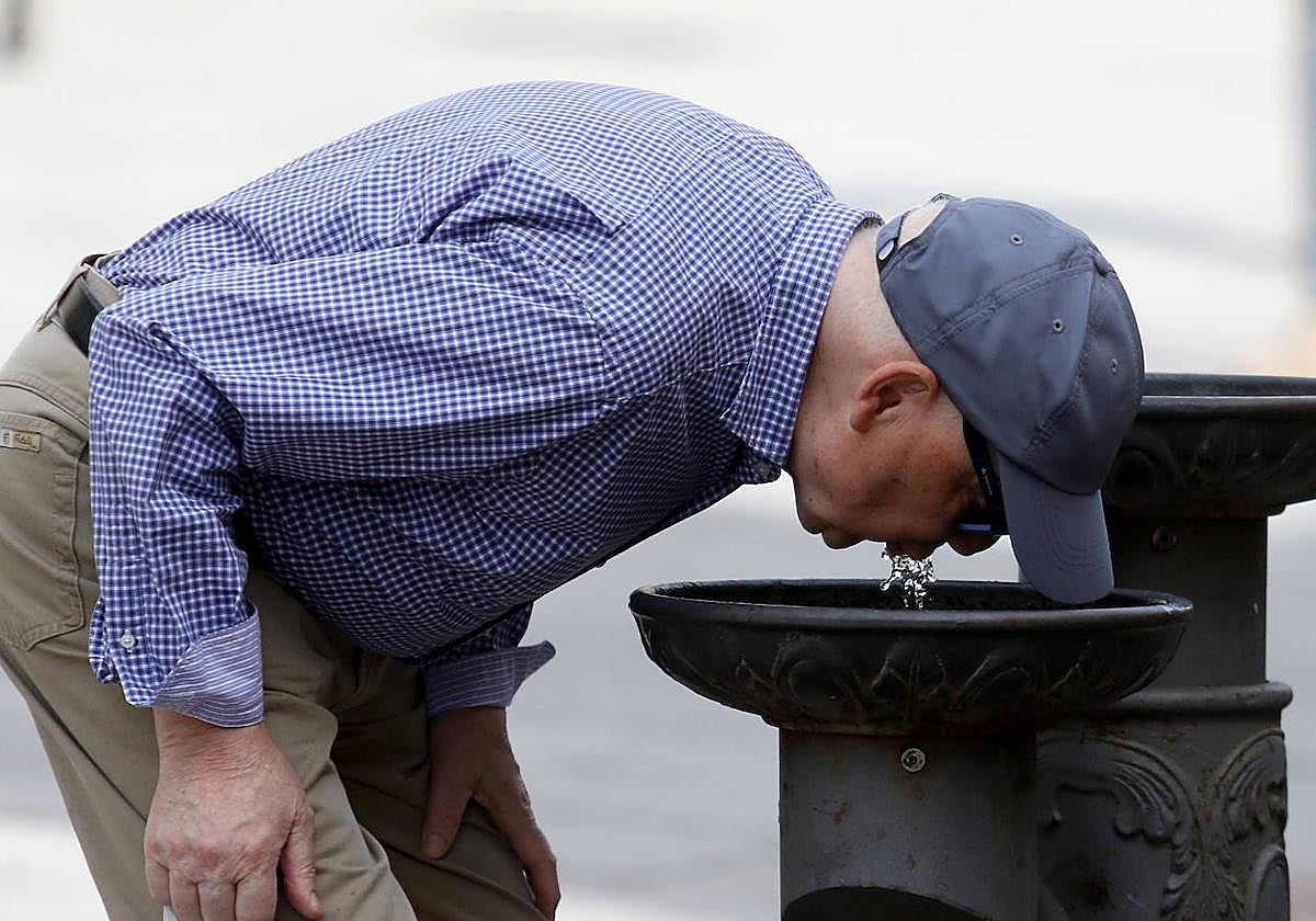 Un hombre bebe agua en una fuente en verano en Segovia.