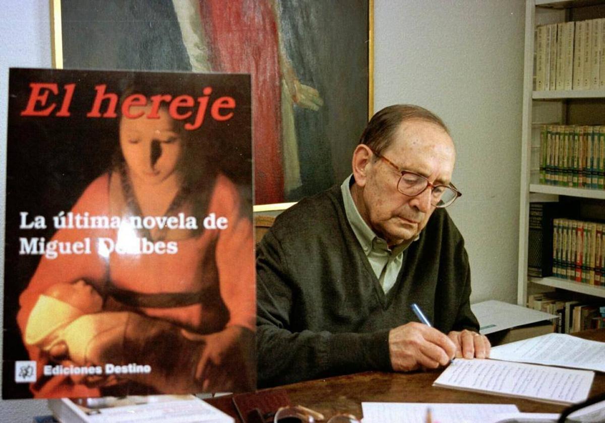 Miguel Delibes, escribiendo en su mesa junto a la portada original de 'El hereje'.