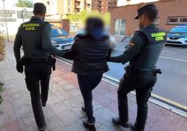 La madre detenida, esposada, es escoltada hasta un vehículo por dos guardias civiles.