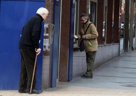 Un hombre saca dinero de un cajero mientras otro espera su turno.