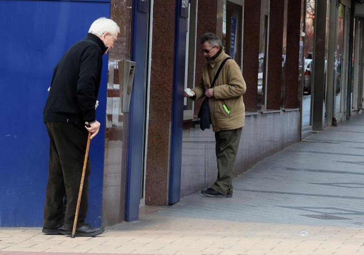 Un hombre saca dinero de un cajero mientras otro espera su turno.