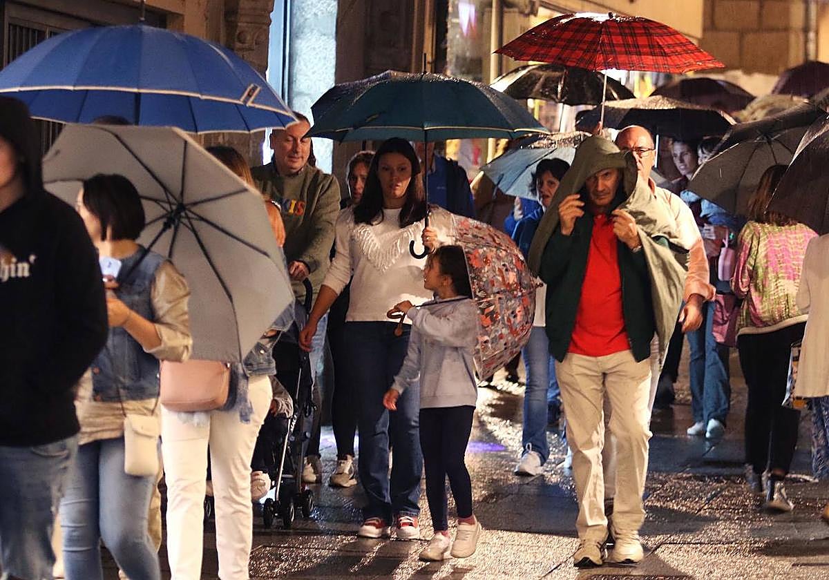 Varios grupos de personas se protegen de la lluvia en la Calle Real de Segovia.