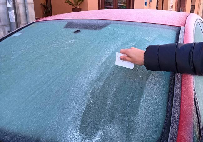 Una mujer trata de quitar el hielo de la luna de su vehículo.