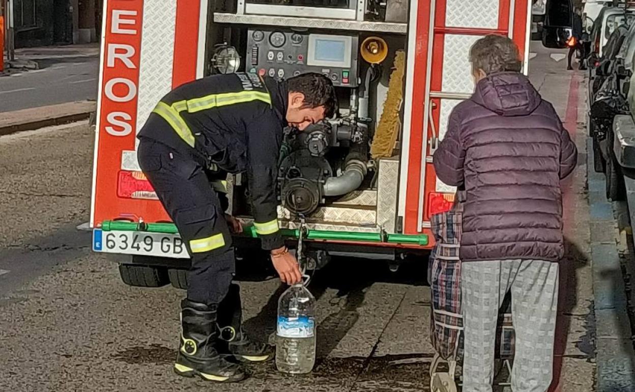 Un bombero llena una garrafa de agua a una vecina afectada por la avería. 