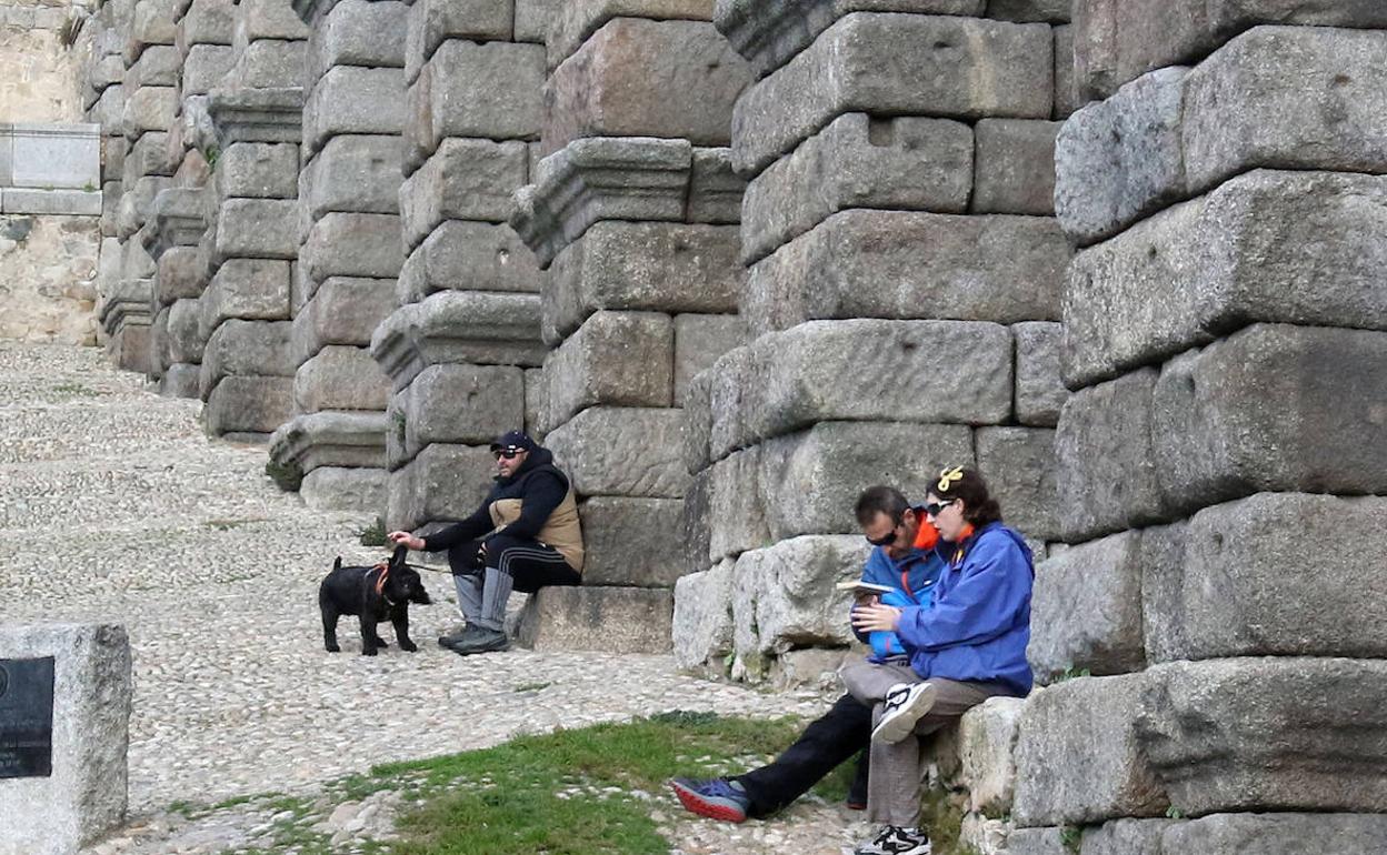 Varias personas descansan apoyadas sobre los sillares del Acueducto.