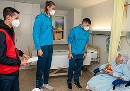 Chumi Ortega entrega un peluche a Valentina, paciente de la octava planta del Río Carrión, mientras Matt Haarms sujeta la caja de muñecos.