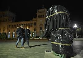 Dos personas, junto a la estatuilla tapada con plásticos instalada en plaza de Zorrilla.