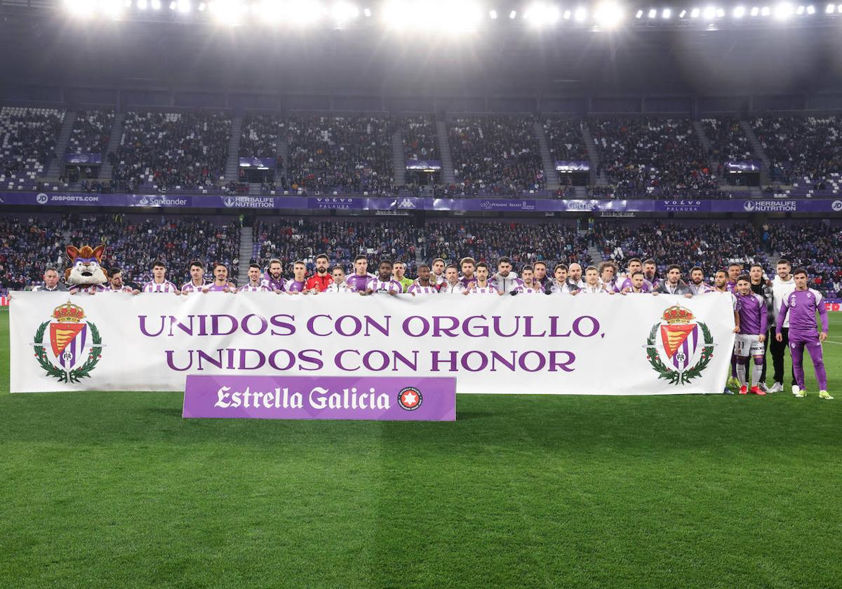 La plantilla blanquivioleta despliega una pancarta con el escudo antiguo antes del partido.