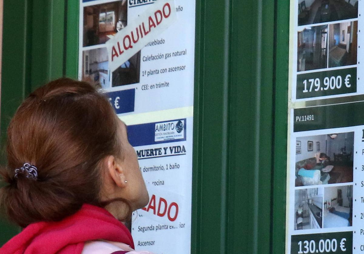 Una mujer observa carteles de venta y alquiler de pisos.