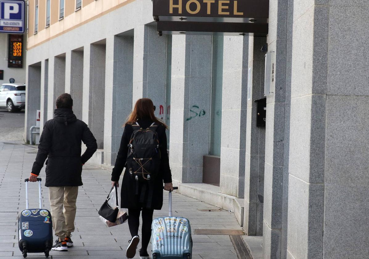 Dos turistas pasan con sus maletas por delante de un hotel de la capital segoviana.