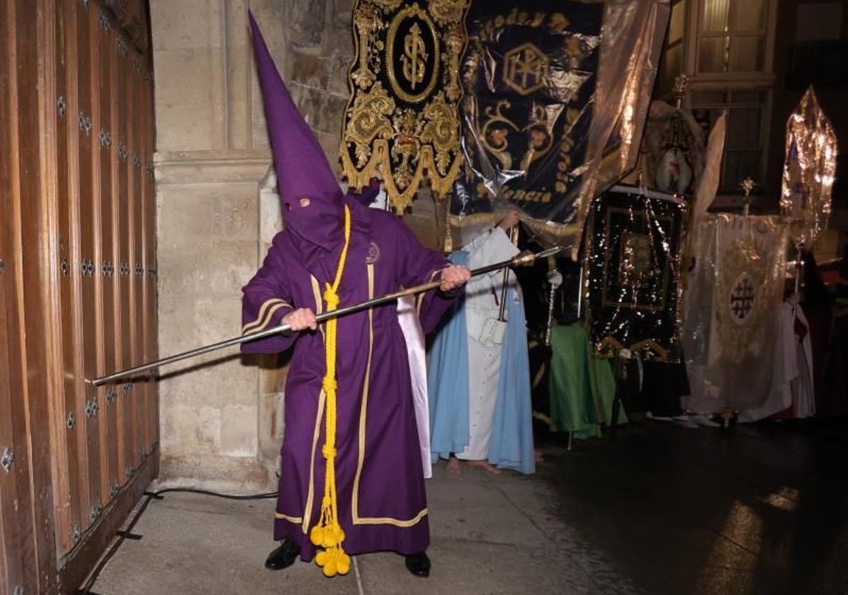 Un nazareno golpea las puertas de San Miguel, junto a los estandartes cubiertos por plásticos.