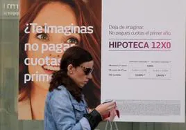 Imagen de archivo de una mujer frente a una entidad bancaria que anuncia sus precios para hipotecas.