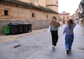 Dos jóvenes pasean junto a los contenedores de la calle Marqués del Arco.