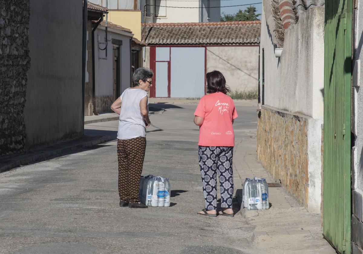 Dos mujeres conversan mientras transportan sus botellas de agua en un municipio segoviano.