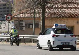 Un coche de prácticas de una autoescuela de Segovia supervisa a un motorista.