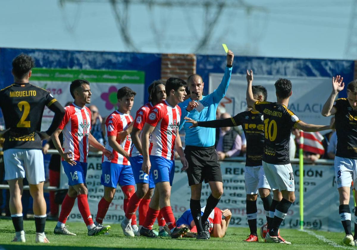 El colegiado muestra una amarilla a un jugador visitante.