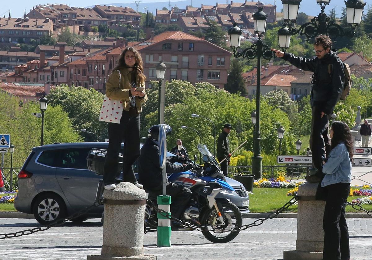 Unos turistas se toman unas fotos subidos en unos bolardos en Segovia.