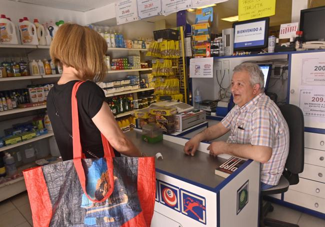 Juan Jesús Potente atiende a una clienta en su tienda de alimentación y despacho de lotería El Faro.