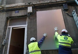 Dos operarios colocan una chapa metálica en una de las ventanas del número 4 de la calle Olmedo.