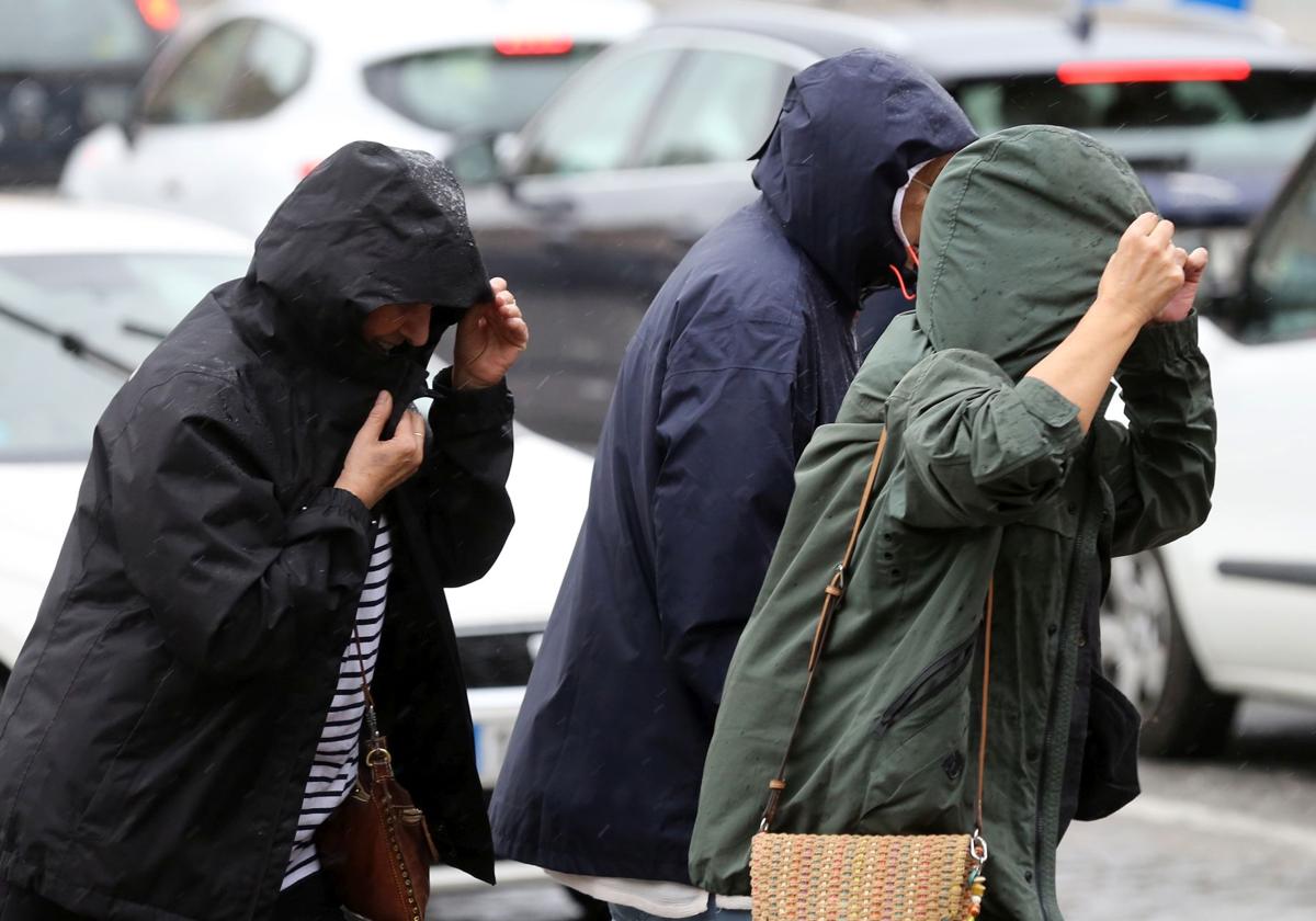 Un grupo de viandantes se protege de la lluvia con abrigos y capuchas.