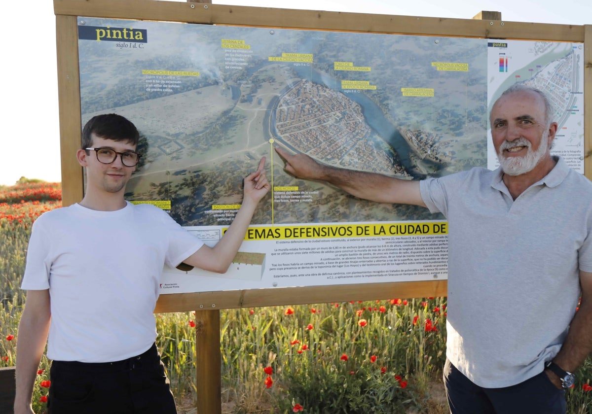 Iván Cuervo -izquierda- junto a Carlos Sanz muestran la recreación 3D de Pintia en uno de los carteles del yacimiento, el ubicado a la entrada de la ciudad.