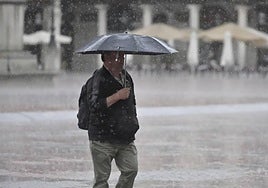 Un hombre intenta resguardarse de la lluvia con un paraguas en la Plaza Mayor Valladolid