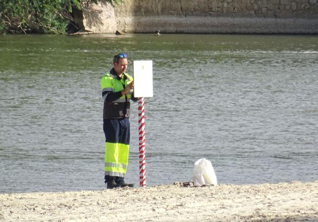 Un operario municipal encinta uno de los postes, que luce el cartel de prohibido bañarse, en la playa de Las Moreras.