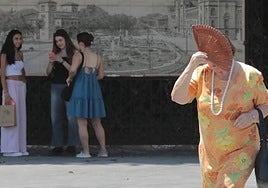 Una mujer se protege del calor con un abanico mientras camina por la plaza de Zorrilla.
