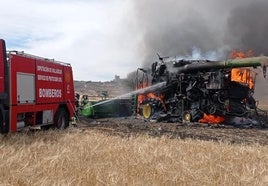 Los bomberos apagan el fuego originado en la cosechadora.