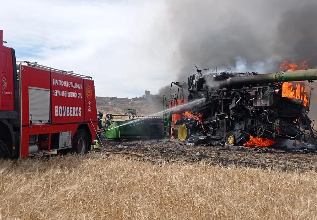 Los bomberos apagan el fuego originado en la cosechadora.