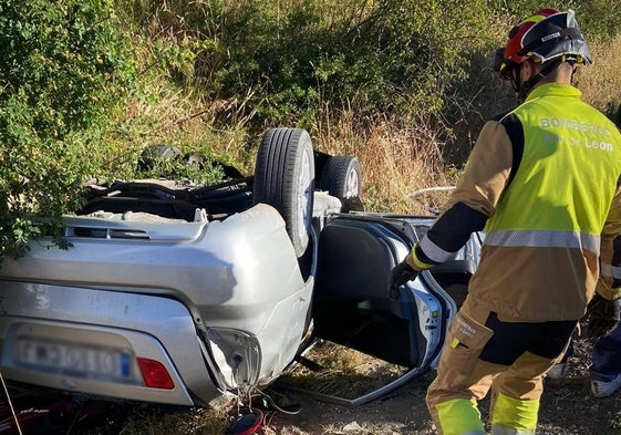 Un miembro de los Bomberos de León, junto al vehículo volcado.