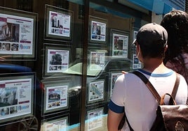 Unos jóvenes consultan los anuncios en el escaparate de una inmobiliaria.
