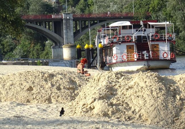 Una mujer toma el sol detrás de un montón de arena en la playa de Las Moreras.