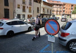 Una hombre circula en patinete junto a una señal que prohíbe el aparcamiento en la plaza de Día Sanz.