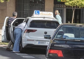 Una alumna se sube a un coche de autoescuela junto a su profesor.